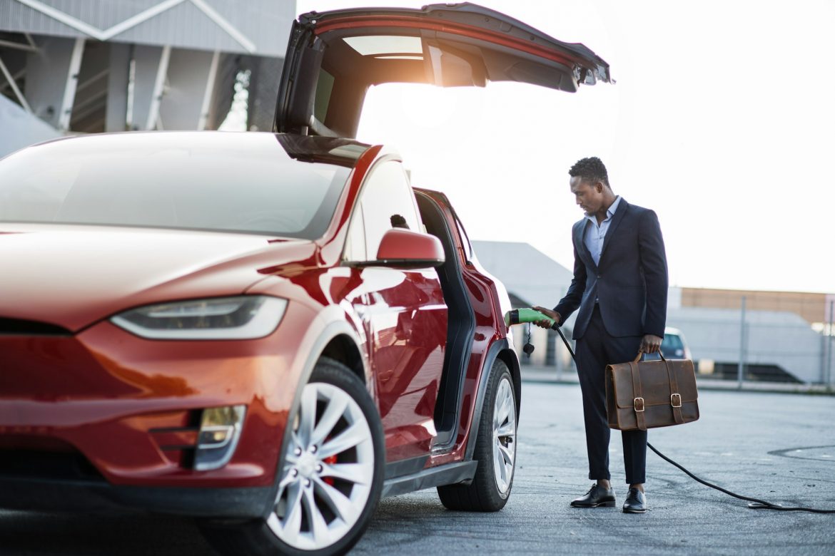 African businessman with suitcase charging electric car السيارات الكهربائية: هل هي مستقبل النقل أم مجرد بديل مؤقت؟