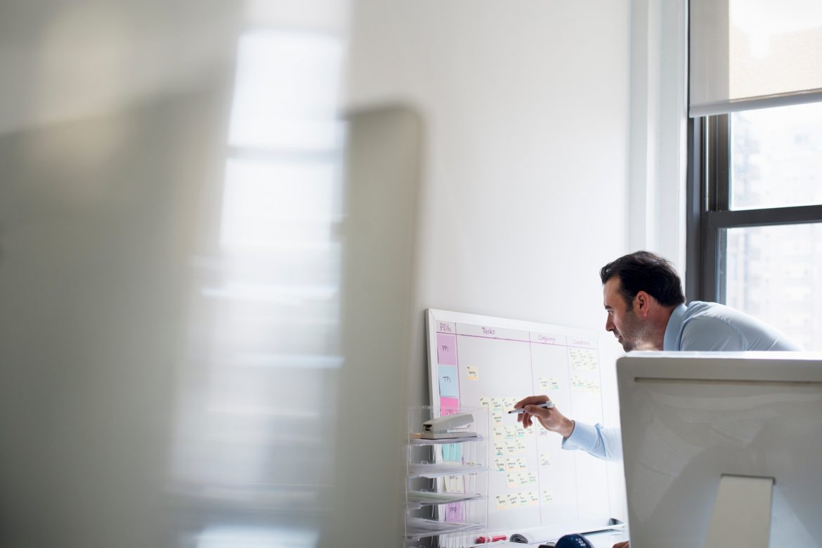 A man using a pen to mark a wall chart or project plan on an office wall.