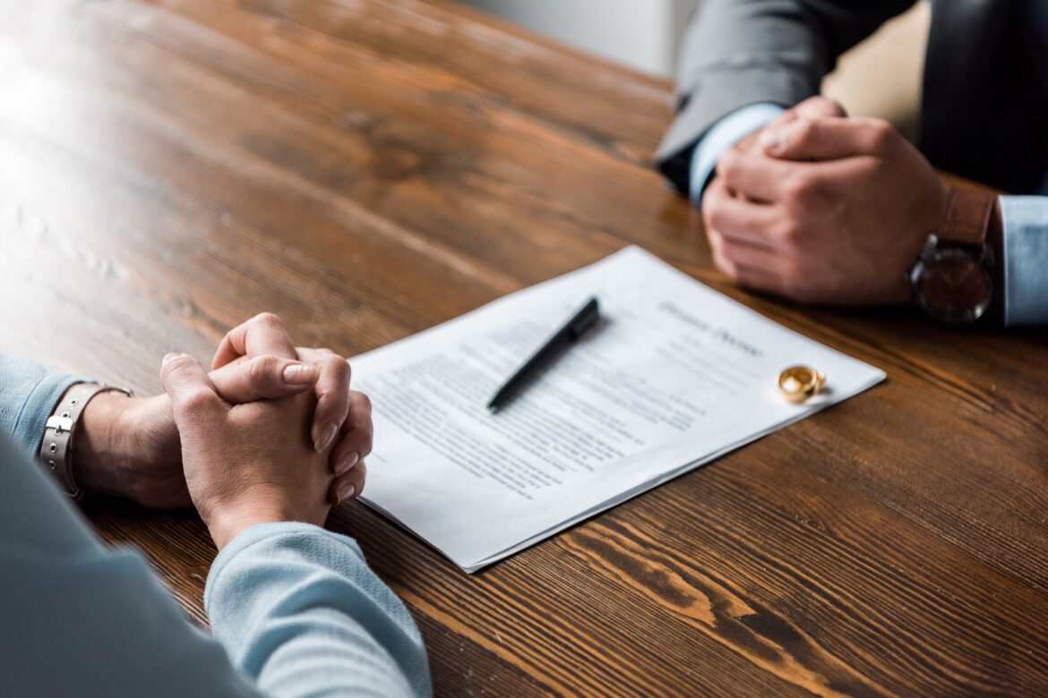 partial view of hands of lawyer and client, divorce decree and wedding rings on table