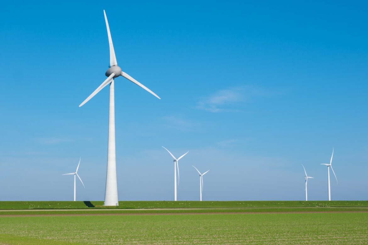 A group of wind turbines gracefully spin in a vast green field, harnessing the power of the wind to