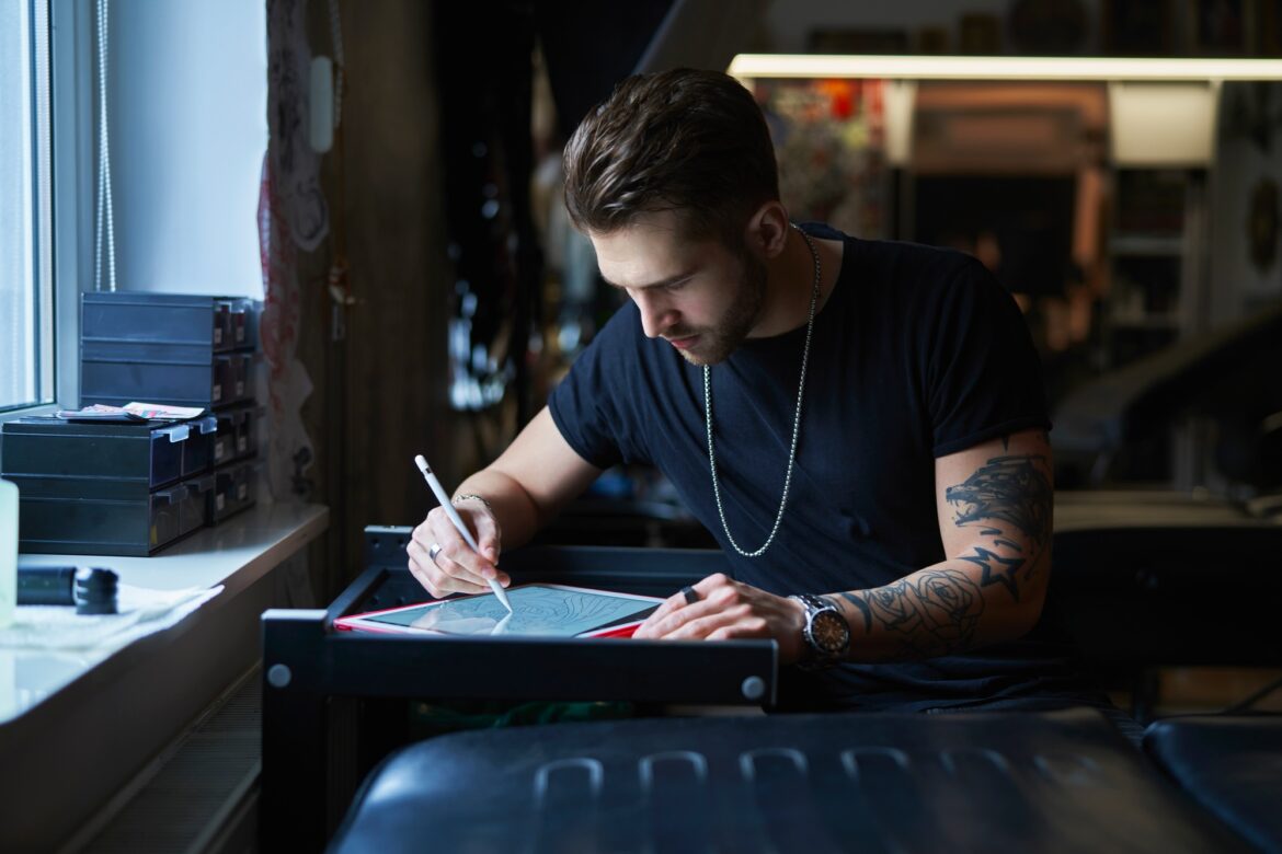 Caucasian tattoo artist designing motifs on digital tablet