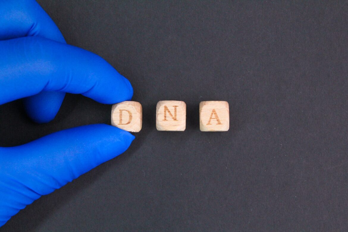 fingers holding a wooden cube with DNA letters.