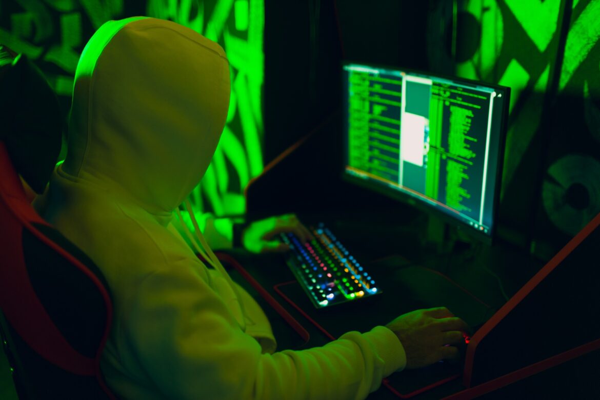 Hacker in hoodie working hacks code site on personal computer with green light