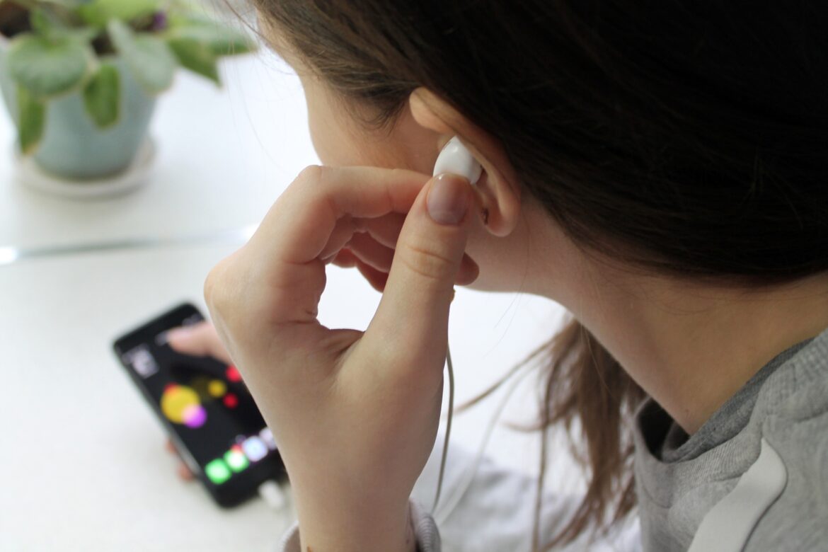 The girl puts an earpiece in her ear and turns on the app on her smartphone