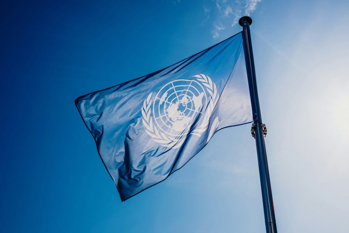 UN flag waved against the sun and blue sky.