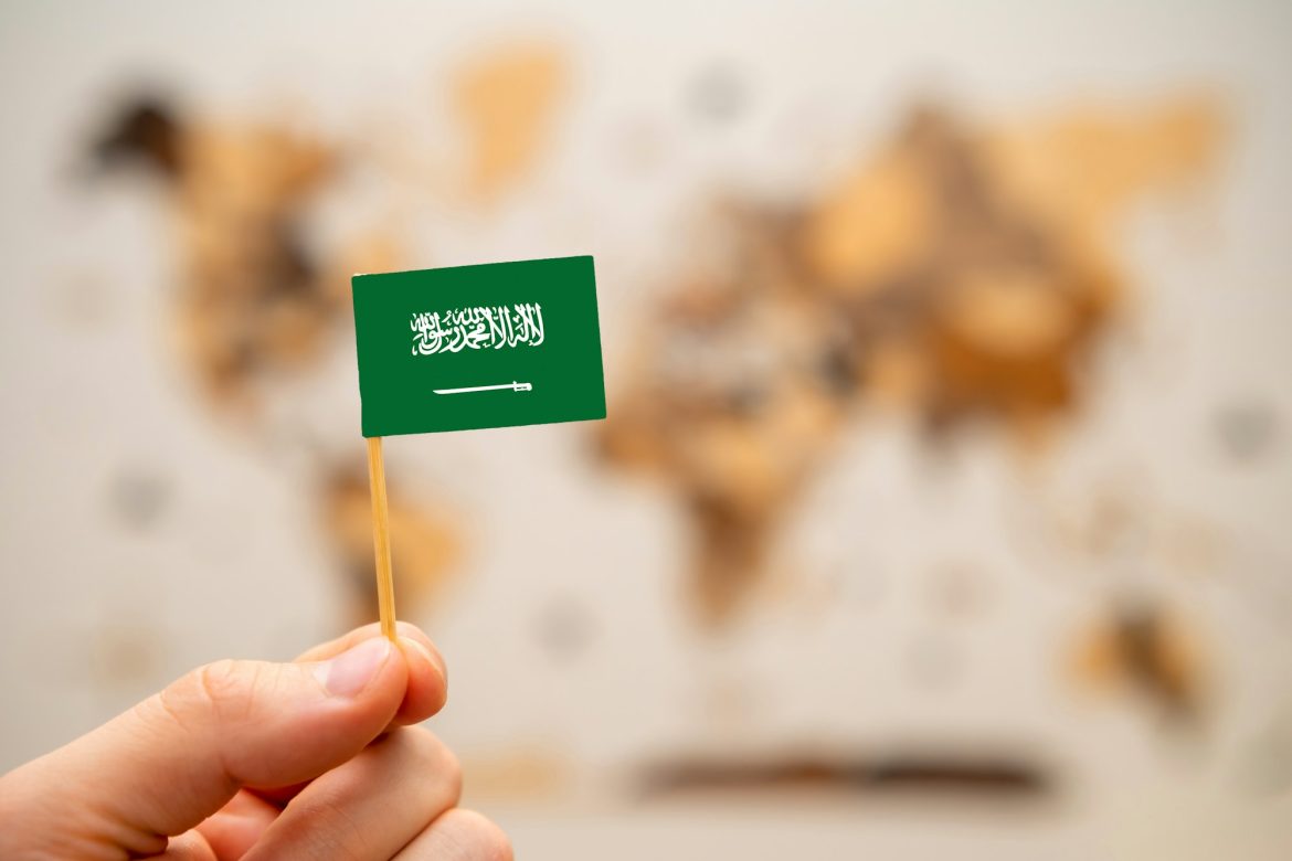 Saudi Arabia flag in mans hand on the world map background.
