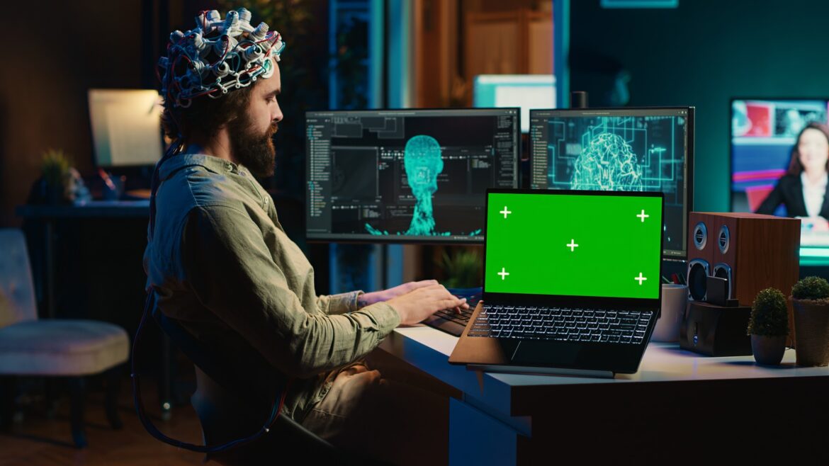 Engineer with EEG headset on merging with AI, green screen laptop