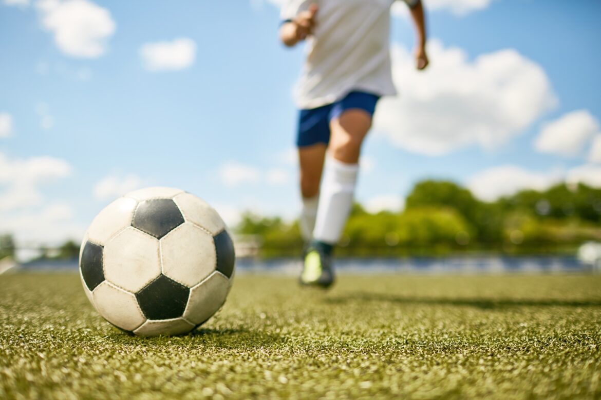 Boy Kicking Ball in Football Field