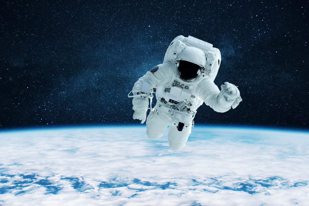 Cool astronaut in a white space suit with a helmet is flying in outer space over the earth
