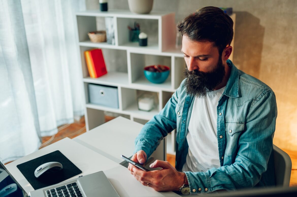 Portrait of a bearded IT expert sitting at his home office and developing a mobile app.